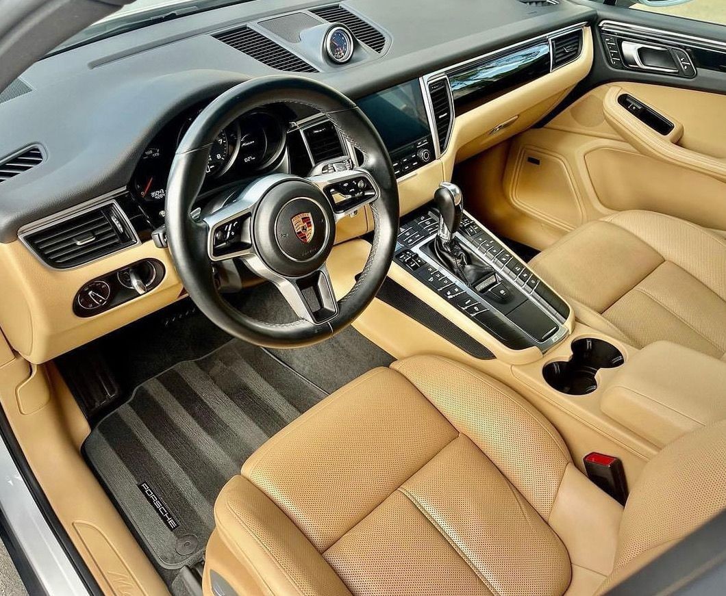 Luxury car interior with tan leather seats, black steering wheel with emblem, and modern dashboard controls.