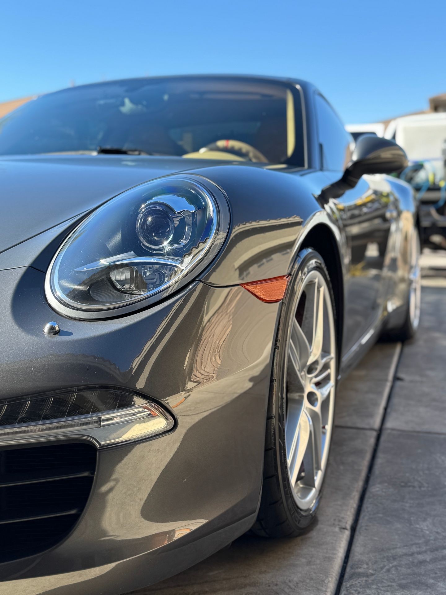 Front view of a sleek, gray sports car with shiny wheels parked on a sunlit driveway.